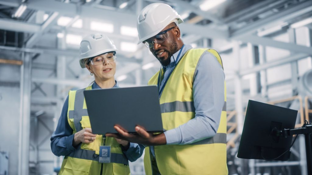 Male and female wearing hard hat using laptop